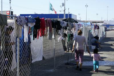 Migrantes caminan a lo largo de una cerca en un campamento improvisado que es hogar temporal de cientos de migrantes que esperan solicitar asilo en Estados Unidos en un cruce peatonal el 8 de noviembre de 2021, en Tijuana, México. (AP Foto/Gregory Bull, Archivo)