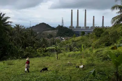 ARCHIVO - Una mujer guía a sus cabras con la planta de carbón de Suralaya al fondo, en Cilegon, Indonesia, el domingo 8 de enero de 2023. (AP Foto/Dita Alangkara, archivo)