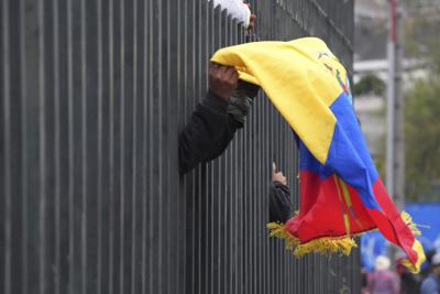 Un manifestante indígena lleva una bandera ecuatoriana dentro de la Casa de la Cultura en Quito mientras policías fuerzan a los manifestantes a quedarse adentro durante una protesta contra el gobierno del presidente Guillermo Lasso el 24 de junio del 2022.  (AP Foto/Dolores Ochoa)