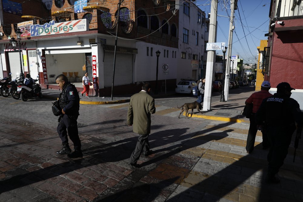 In this Feb. 10, 2020 photo, policemen and pedestrians walk outside town hall in Apaseo el Alto, Guanajuato state, Mexico. Mexico's fastest-rising cartel, the Jalisco New Generation gang, has a reputation for ruthlessness and violence unlike any since the fall of the old Zetas cartel. In states like Guanajuato it is fighting medieval-style battles, complete with fortified redoubts, to expand nationwide, from the outskirts of Mexico City, into the tourist resorts around Cancun, and along the northern border. (AP Photo/Rebecca Blackwell)