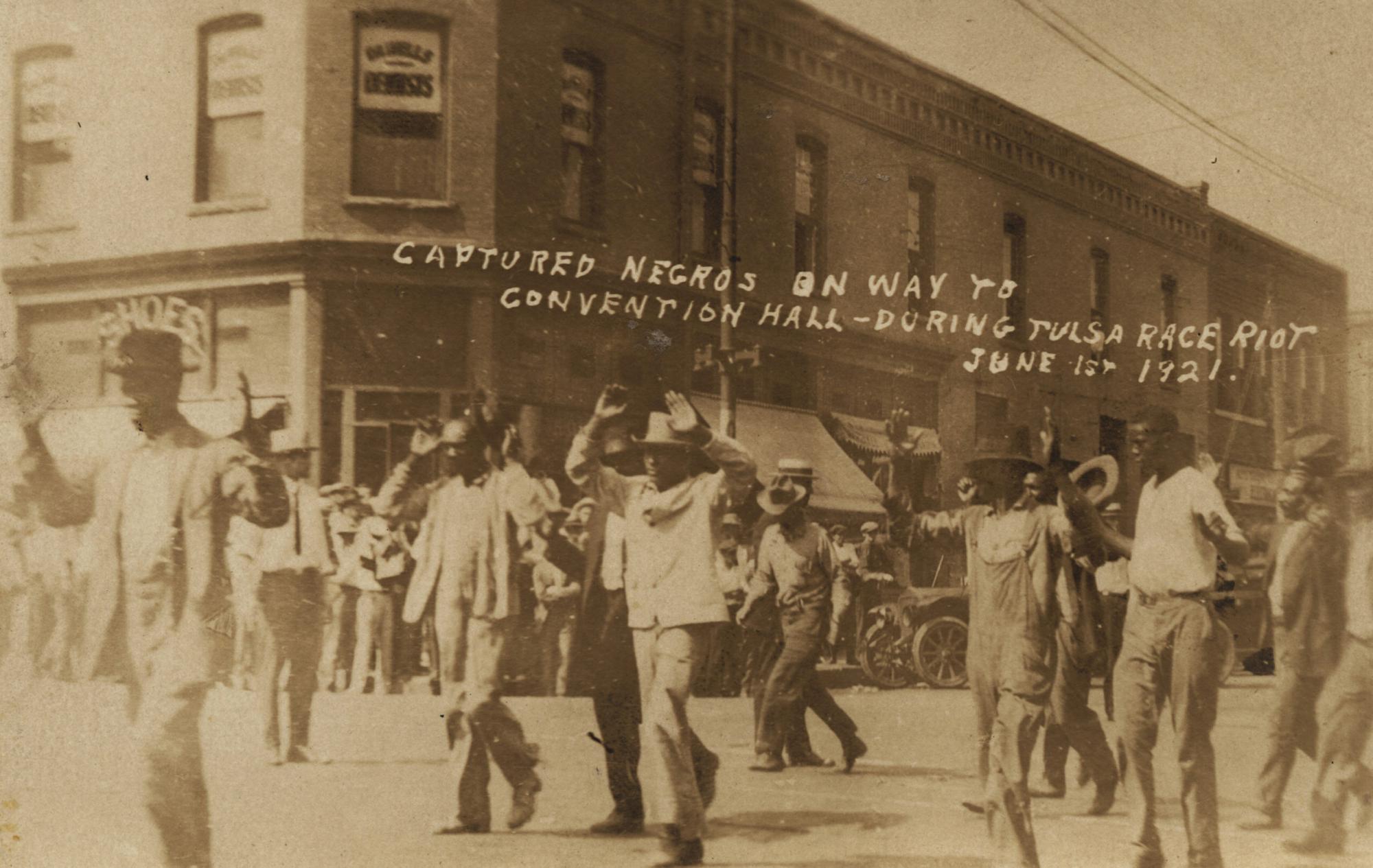 In this photo provided by the Department of Special Collections, McFarlin Library, The University of Tulsa, a group of Black men are marched past the corner of 2nd and Main Streets in Tulsa, Okla., under armed guard during the Tulsa Race Massacre on June 1, 1921. (Department of Special Collections, McFarlin Library, The University of Tulsa via AP)