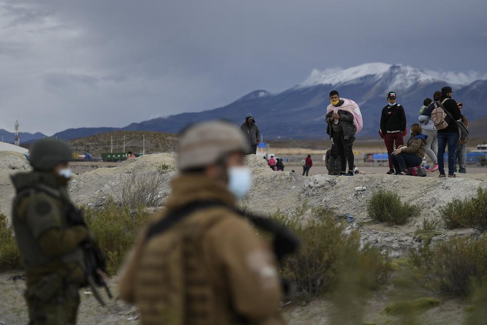 Migrants stand on the Bolivian side of the border as soldiers stand guard on the Chilean side near Colchane, Chile, Thursday, Dec. 9, 2021. (AP Photo/Matias Delacroix)