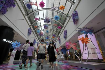 Residentes con máscaras faciales caminan por el centro comercial de reapertura decorado con flores de colores después de haber estado cerrado debido a las restricciones de COVID-19 en Beijing, el domingo 29 de mayo de 2022. (AP Foto/Andy Wong)