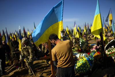 Un hombre coloca una bandera ucraniana en la tumba del militar ucraniano Vadim Bereghnuy, de 22 años, durante su funeral en un cementerio en Járkiv, Ucrania, el lunes 17 de octubre de 2022. (Foto AP/Francisco Seco)
