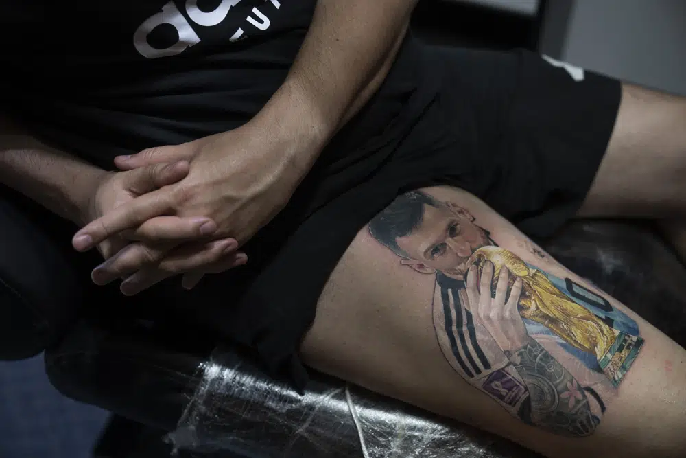 Sebastián Fernández descansa mientras el artista César "Yeyo" Molina le tatúa en la pierna una imagen del futbolista Lionel Messi besando la Copa del Mundo en Buenos Aires, Argentina, el jueves 29 de diciembre de 2022. (AP Foto/Víctor R. Caivano)