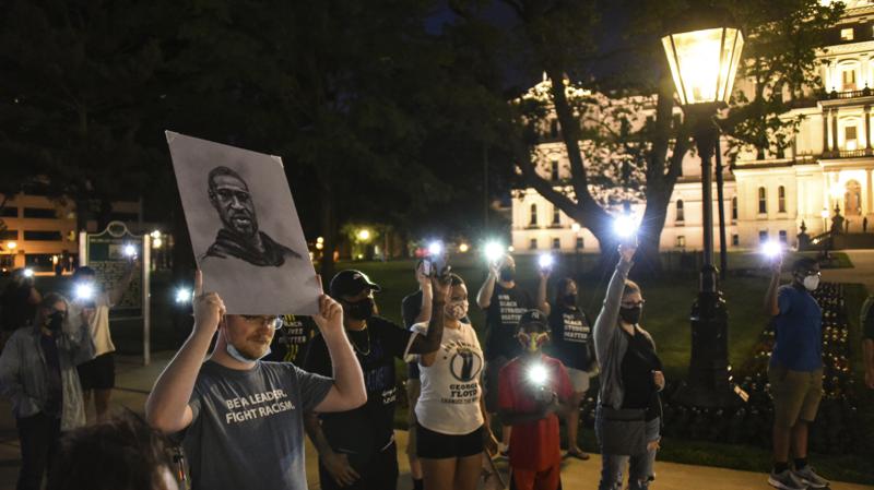 Mitchell Eithun of Lansing, Mich., holds up a sketch of George Floyd created by friend Cheryl Gamber, while others hold up lit cell phones to remember Floyd on Tuesday evening, May 25, 2021, during a memorial at the state Capitol in Lansing, Mich., a year after Floyd's death at the hands of Minneapolis police. The event was sponsored by Black Lives Matter Lansing. (Matthew Dae Smith/Lansing State Journal via AP)