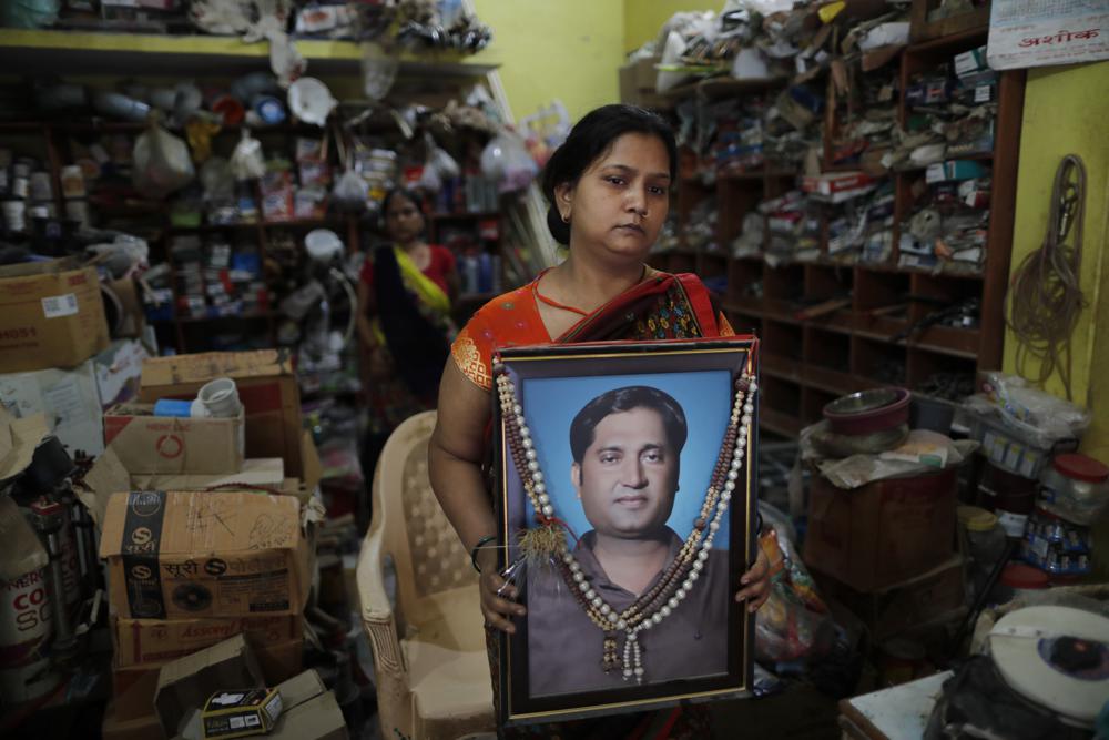 Reena Kesarwani holds a photograph of her husband, Anand Babu Kesarwani, who died of COVID-19, in their hardware shop, Monday, Oct. 25, 2021, in the Chhitpalgarh village, in India's northern Uttar Pradesh state. (AP Photo/Rajesh Kumar Singh)