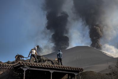 Varias personas limpian la ceniza de un tejado durante la erupción de un volcán en la isla de La Palma, España, el 14 de octubre de 2021. (AP Foto/Saúl Santos)