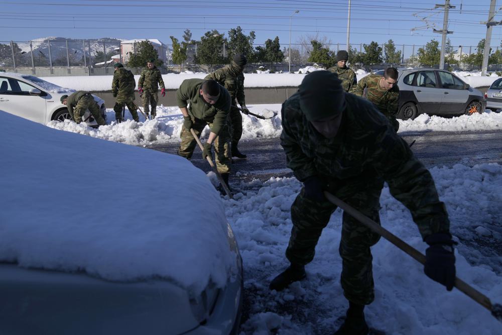 Tripulaciones del ejército intentan retirar vehículos varados en la nieve durante tres días a lo largo de la autopista de peaje Attiki Odos, que une Atenas con el aeropuerto internacional de la capital, Grecia, el miércoles 26 de enero de 2022. oscureció partes de la ciudad.  (Foto AP/Thanassis Stavrakis)