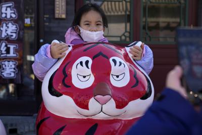 Una niña con mascarilla se agarra a las orejas de una estatua de un tigre en el primer día del Año Nuevo lunar del Tigre, en Beijing, China, el 1 de febrero de 2022. (AP Foto/Ng Han Guan)