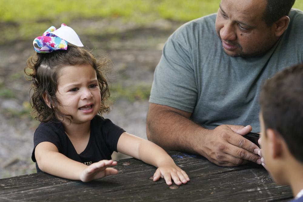 Víctor Macedo y su hijo, José Antonio, escuchan a Sonia, de tres años, mientras visitan un parque el jueves 14 de julio de 2022, en Sunrise, Florida. La familia huyó de Venezuela y en diciembre cruzó la frontera de Estados Unidos con México. Son parte de un numeroso grupo de venezolanos que quedaron afuera de un programa de protección temporal para algunos extranjeros que no han regularizado su situación migratoria, conocido como TPS. El gobierno acaba de extenderlo para los que llegaron antes del 9 de hasta marzo de 2021. (AP Foto/Marta Lavandier)