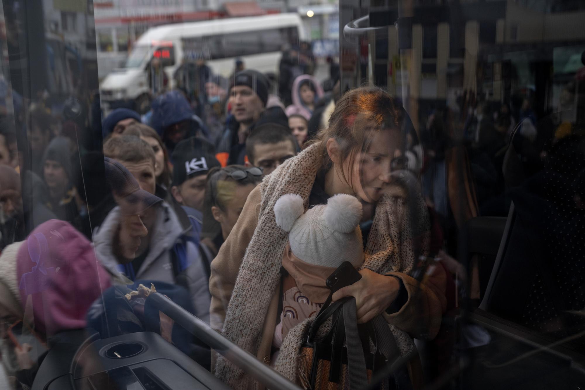 Một người phụ nữ bế con gấp rút lên xe bus rời khỏi Kyiv, Ukraine, ngày 24/02/2022. Ảnh: AP Photo/ Emilio Morenatti