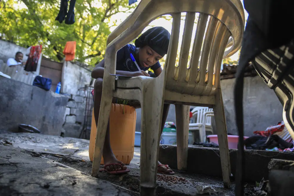 Christina Julien does her homework on a chair in Port-au-Prince, Haiti, Sunday, Jan. 22, 2023. Julien is one of the thousands of people in the capital who has been forced to flee her home due t violence, seeking refuge with family members in another part of the city. (AP Photo/Odelyn Joseph)