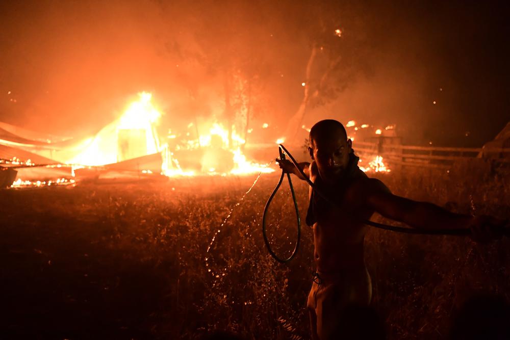 A man uses a water hose during a wildfire in Adames area, in northern Athens, Greece, Tuesday, Aug. 3, 2021.Thousands of people fled their homes north of Athens on Tuesday as a wildfire broke out of the forest and reached residential areas. The hurried evacuations took place just as Greece grappled with its worst heat wave in decades. (AP Photo/Michael Varaklas)