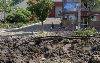 Una mujer camina al lado de un enorme cráter causado por un ataque ruso con misiles en el centro de la ciudad de Bakhmut, en la región de Donetsk, Ucrania, el viernes 1 de julio de 2022. (AP Foto/Efrem Lukatsky)