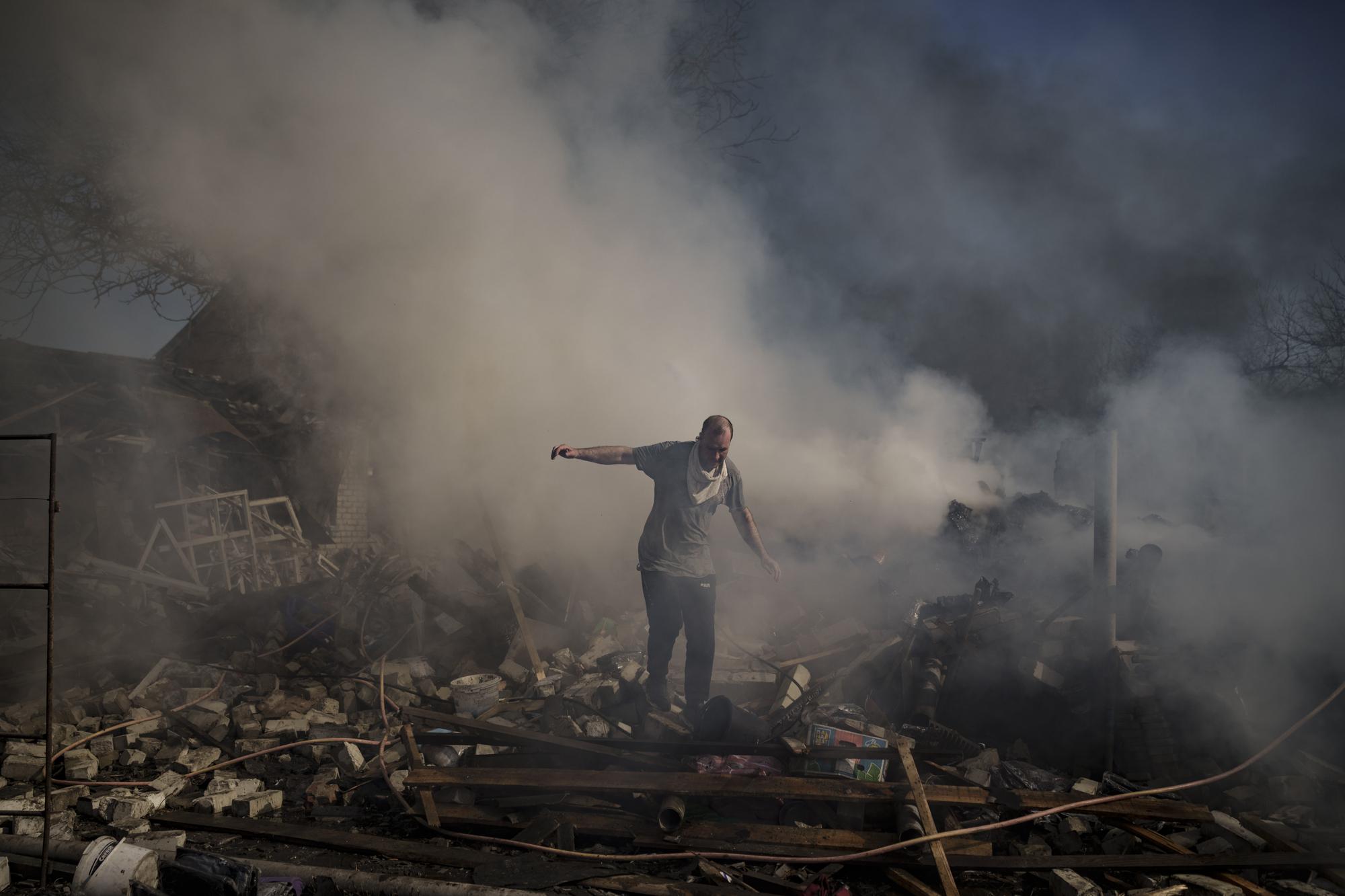 A neighbor walks on the debris of a burning house, destroyed after a Russian attack in Kharkiv, Ukraine, Thursday, March 24, 2022. (AP Photo/Felipe Dana)