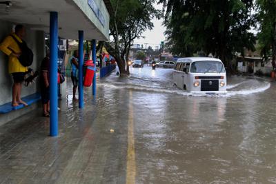 Una mujer se para en el banco de una parada de autobús mientras el conductor de una camioneta Volkswagen navega por una calle inundada en Recife, estado de Pernambuco, Brasil, el sábado 28 de mayo de 2022. (AP Photo/Marlon Costa/Futura Press)