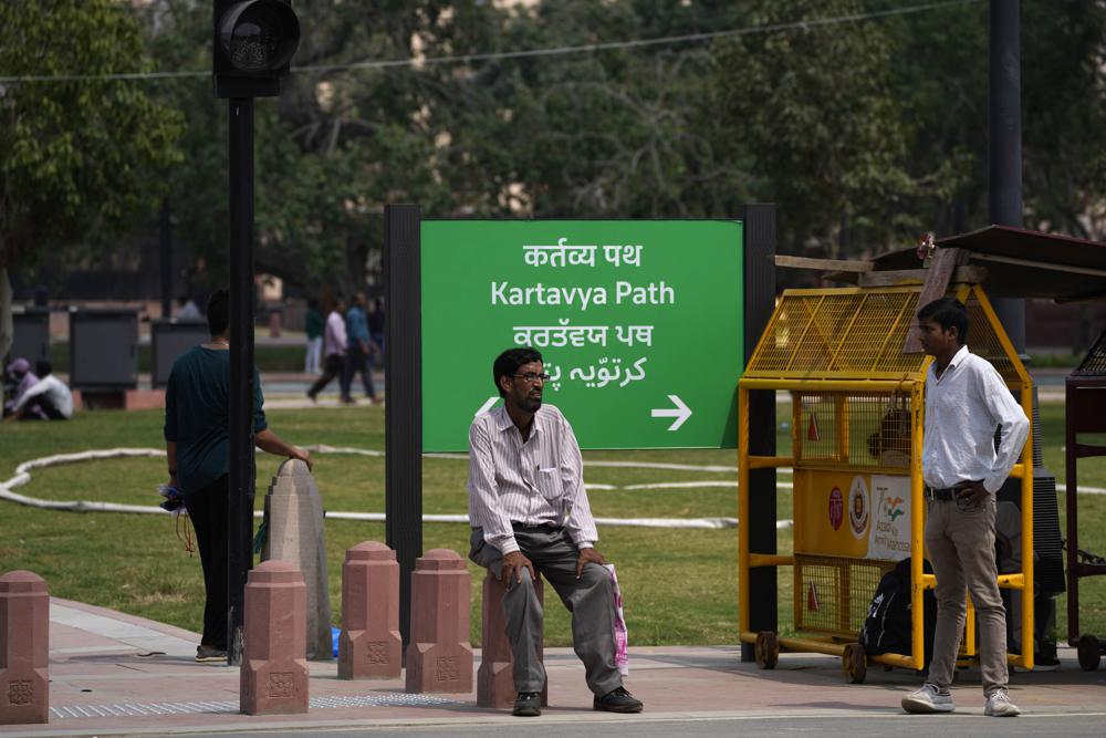 A man rests on a newly constructed pillar in front of a road signage which is changed from Rajpath to Kartavya Path, in New Delhi. (Photo: Manish Swarup/AP)