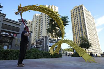 Una persona hace ondear un dragón de tela ante el complejo residencial Evergrande Yujing Bay en Beijing, China, el martes 21 de septiembre de 2021. Inversionistas de todo el mundo seguían las noticias con nerviosismo mientras una de las mayores promotoras de bienes raíces de China trataba de evitar la suspensión de pagos en deudas multimillonarias, lo que podría tener amplios efectos en el sistema financiero. (AP Foto/Ng Han Guan)