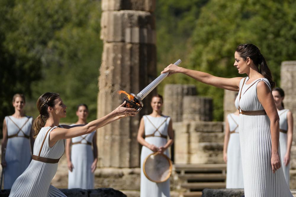 La actriz griega Xanthi Georgiou (derecha) sostiene la antorcha durante el encendido de la llama de los Juegos Olímpicos de Invierno Beijing 2022, el lunes 18 de octubre de 2021, en Olimpia Antigua. (AP Foto/Thanassis Stavrakis)