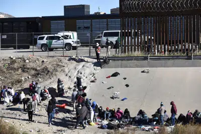 Migrantes esperan a cruzar la frontera entre Estados Unidos y México, el miércoles 14 de diciembre de 2022, desde Ciudad Juárez, México, frente a vehículos de la Patrulla Fronteriza en El Paso, Texas. (AP Foto/Christian Chávez)