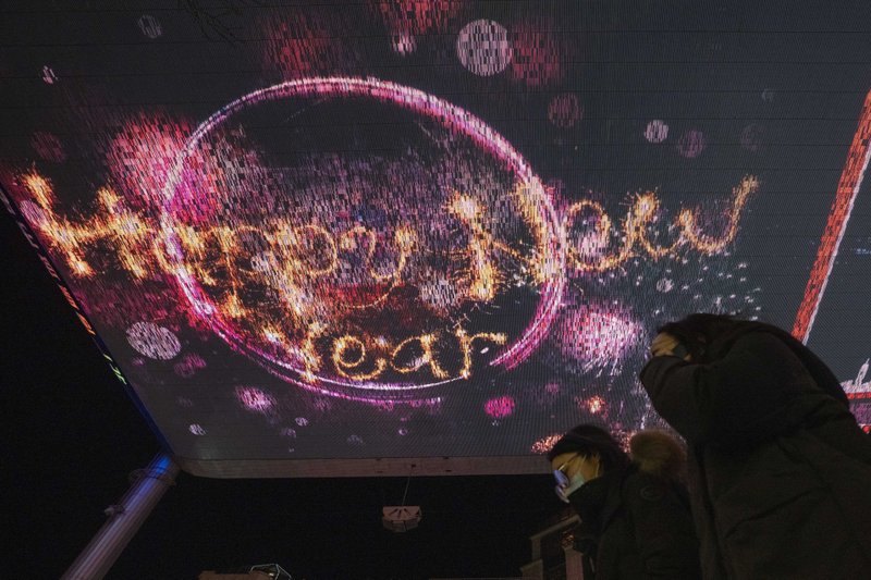 Visitors to a mall passes by Happy New Year greetings shown on a giant screen in Beijing Thursday, Dec. 31, 2020. This New Year's Eve is being celebrated like no other, with pandemic restrictions limiting crowds and many people bidding farewell to a year they'd prefer to forget. (AP Photo/Ng Han Guan)