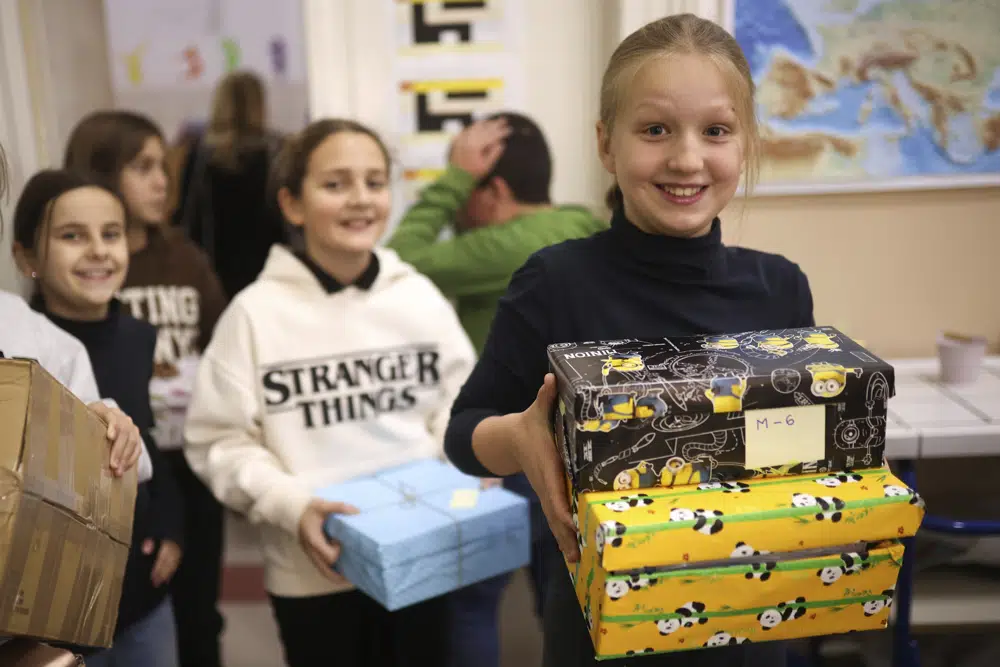 Bosnian children carry holiday presents for Ukrainian children at Safvet Beg Basagic elementary school in Sarajevo, Bosnia, Tuesday, Dec. 20, 2022. In homes and schools around Bosnia, youngsters have been preparing gift boxes they hope will put a smile on the faces of their peers living through war in Ukraine. For parents and educators helping the kids select what to send, the experience has awakened a rare found memory of the time when they were on the receiving end of the kindness of strangers while growing up and living in constant fear of death. (AP Photo/Armin Durgut)