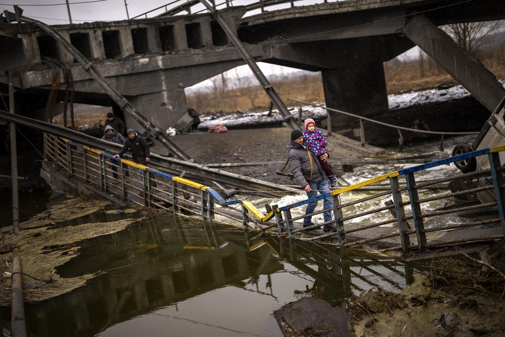 La combatiente Valery, de 37 años, carga a un niño mientras ayuda a una familia a cruzar un puente que fue destruido por artillería, el miércoles 2 de marzo de 2022, en Kiev. (AP Foto/Emilio Morenatti)