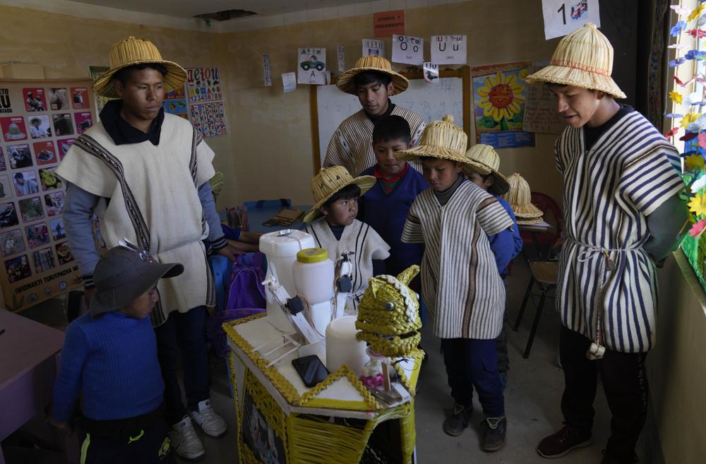 Estudiantes del grupo indígena Irohito Urus observan un robot hecho con materiales reciclados en un salón de clases en Irohito Urus, Bolivia, el jueves 21 de abril de 2022. Tres estudiantes crearon el robot utilizando materiales de su entorno, como cañas, para desinfectar superficies como teléfonos celulares y crear conciencia para combatir el COVID-19. (AP Foto/Juan Karita)