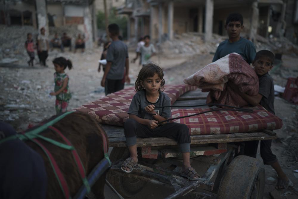 Chadi Nassir, de 7 siete años, se sienta en un carro tirado por un burro mientras su hermano, Mahmoud, lo carga con pertenencias recuperadas de su casa dañada en Beit Hanoun, en el norte de la Franja de Gaza, el domingo 13 de junio de 2021. (AP Foto/Felipe Dana)