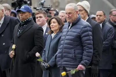 De izquierda a derecha, el alcalde neoyorquino Eric Adams; la gobernadora del estado de Nueva York, Kathy Hochul, y el líder de la mayoría demócrata en el Senado, Chuck Schumer, aguardan para colocar flores sobre los nombres de las víctimas del atentado de 1993 contra el Centro Mundial de Comercio, durante una ceremonia en el monumento conmemorativo a los atentados del 11 de septiembre de 2001, el domingo 26 de febrero de 2023, en Nueva York. (AP Foto/John Minchillo)