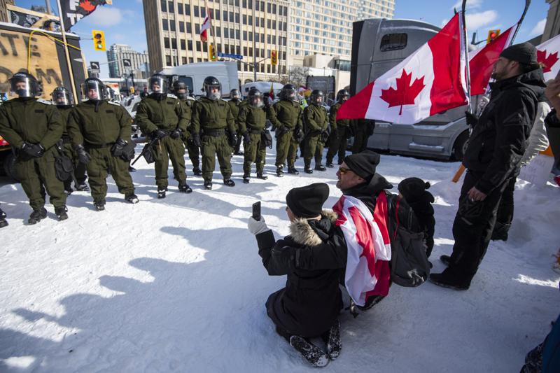 Protesters kneel in front of Surete du Quebec officers forming an enclosure around blockaded vehicles on Rideau Street, as police aim to end an ongoing protest against COVID-19 measures that has grown into a broader anti-government protest, in Ottawa, Ontario, Friday, Feb. 18, 2022. (Justin Tang/The Canadian Press via AP)