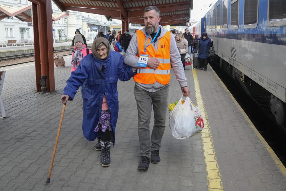 A volunteer helps an elderly Ukrainian refugee walk along a platform at a railway station in Przemysl, Poland, on Friday, March 25, 2022. (AP Photo/Sergei Grits)