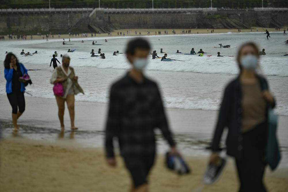 FILE - In this May 9, 2021, file photo, people walk along La Concha beach, after lockdown restrictions were lifted, in San Sebastian, northern Spain. Coronavirus infections, hospitalizations and deaths are plummeting across much of Europe. Vaccination rates are accelerating, and with them, the promise of summer vacations. (AP Photo/Alvaro Barrientos, File)