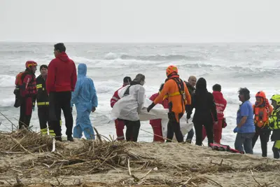 Rescatistas recuperan un cadáver de una playa cercana a Cutro, en el sur de Italia, el domingo 26 de febrero de 2023, después de que un bote de migrantes se partió en un mar picado. (AP Foto/Giuseppe Pipita)