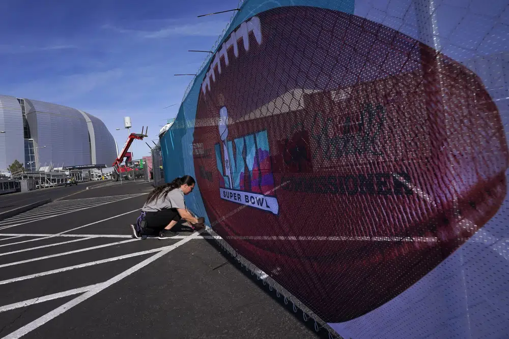 Eilish GrayWoulfe covers a fence with graphics outside State Farm Stadium, Friday, Feb. 3, 2023, in Glendale, Ariz. in preparation for the NFL Super Bowl LVII football game on Feb 12. (AP Photo/Matt York)