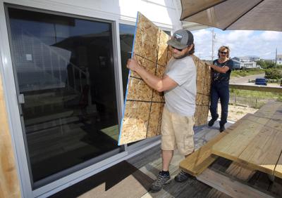 James Masog, al centro, y Gary Tavares, llevan una tabla de conglomerado para proteger las puertas de vidrio de la casa de un cliente en Charlestown, Rhode Island, antes de la llegada del huracán Henri, e sábado, 21 de agosto del 2021. (AP Foto/Stew Milne)