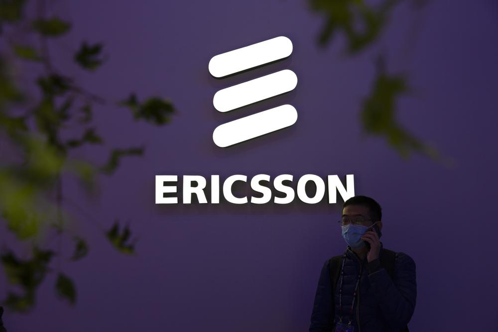 FILE - A man wearing a face mask talks on his smartphone near a booth from Swedish technology firm Ericsson at the PT Expo in Beijing, Wednesday, Oct. 14, 2020. Swedish telecom equipment maker Ericsson has agreed to plead guilty to U.S. foreign corruption violations and pay more than $206 million for breaking a deal with the Justice Department over charges of bribery and falsifying records in countries from China to Kuwait. (AP Photo/Mark Schiefelbein, File)