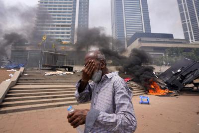 Un hombre reacciona a los gases lacrimógenos mientras camina frente a un campamento destrozado de manifestantes antigubernamentales frente a la oficina del presidente en Colombo, Sri Lanka, el lunes 9 de mayo de 2022. (Foto AP/Eranga Jayawardena)