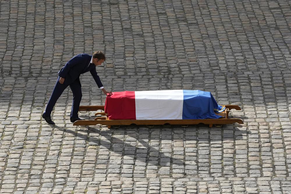 French President Emmanuel Macron touches the coffin of Jean-Paul Belmondo during a tribute ceremony for the late French actor at the Hotel des Invalides, Thursday, Sept.9 2021 in Paris. The tributes for the star of iconic French New Wave film "Breathless" reflect his prominent role in France's cultural world and in living rooms, where families gathered around his films. Belmondo, whose crooked boxer's nose and rakish grin made him one of the country's most recognizable leading men, died at 88 earlier this week. (AP Photo/ Michel Euler)
