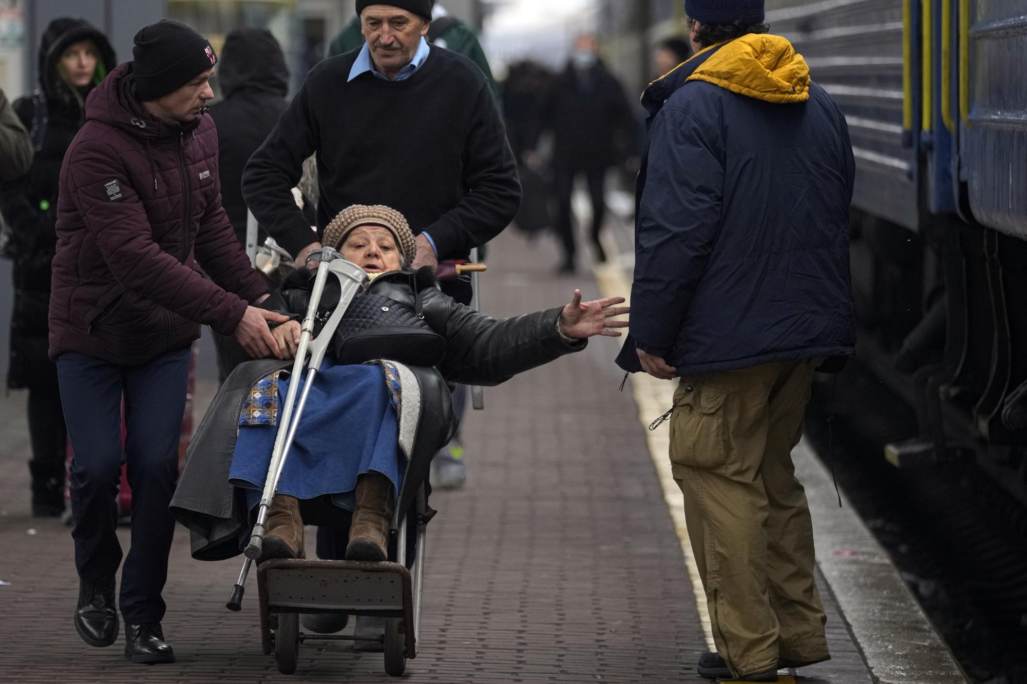 Men push a luggage trolley carrying an elderly lady before boarding a Lviv bound train, in Kyiv, Ukraine, Thursday, March 3, 2022. (AP Photo/Vadim Ghirda)