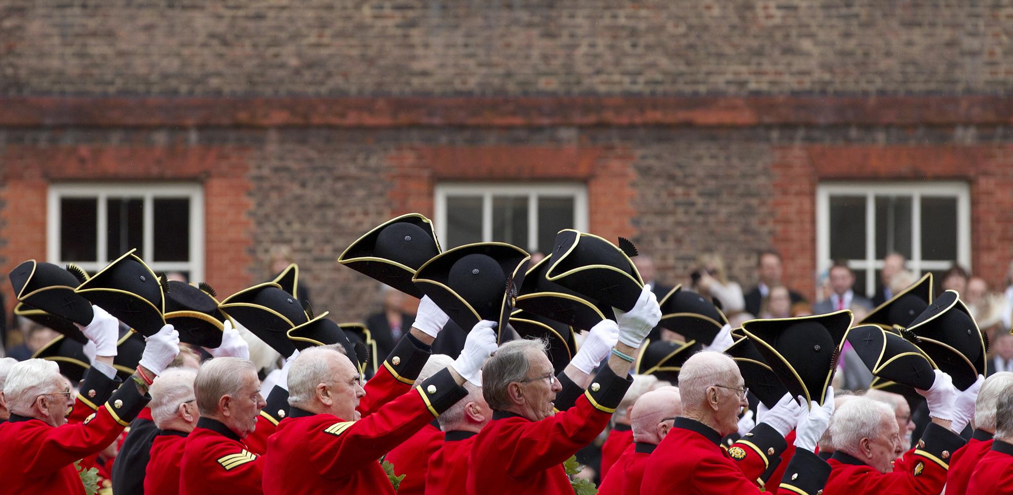 FILE - Chelsea Pensioners raise their hats as they offer three cheers for Britain's Queen Elizabeth II, as they take part in their Founders Day parade in London, Thursday, June 7, 2012. The Royal Hospital Chelsea has been caring for Britain's veteran soldiers since its foundation by King Charles II in 1682, the veterans known as Chelsea Pensioners are easily identifiable by their traditional red coats. (AP Photo/Alastair Grant, File)