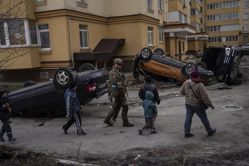 Un soldado ucraniano camina con niños pasando autos destruidos por la guerra contra Rusia, en Bucha, en las afueras de Kiev, Ucrania, el lunes 4 de abril de 2022. (Foto AP/Rodrigo Abd)