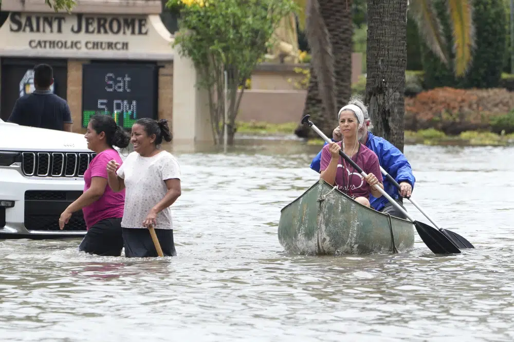 Residents paddle and walk along a flooded road Thursday, April 13, 2023, in Fort Lauderdale, Fla. Over two feet of rain fell causing widespread flooding, closing the Fort Lauderdale airport and turning thoroughfares into rivers. (AP Photo/Marta Lavandier)