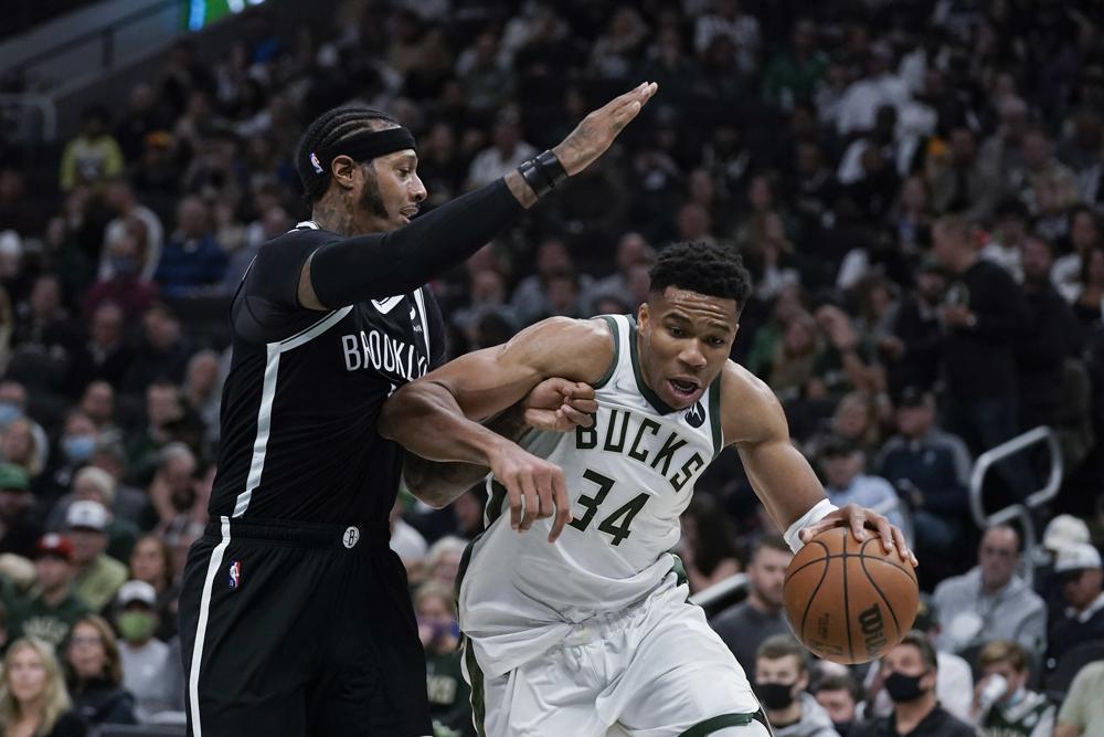 Giannis Antetokounmpo (34), de los Bucks de Milwaukee, es defendido por James Johnson, de los Nets de Brooklyn, durante la primera mitad del juego de la NBA, el martes 19 de octubre de 2021, en Milwaukee. (AP Foto/Morry Gash)