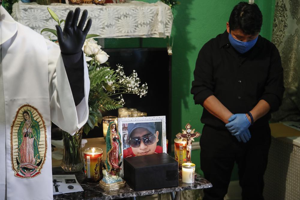 FILE - In this May 9, 2020, file photo, the Rev. Fabian Arias, left, performs an in-home service beside the remains of Raul Luis Lopez who died from COVID-19 the previous month as Lopez's cousin Miguel Hernandez Gomez, right, bows his head in prayer in the Corona neighborhood of the Queens borough of New York. (AP Photo/John Minchillo, File)