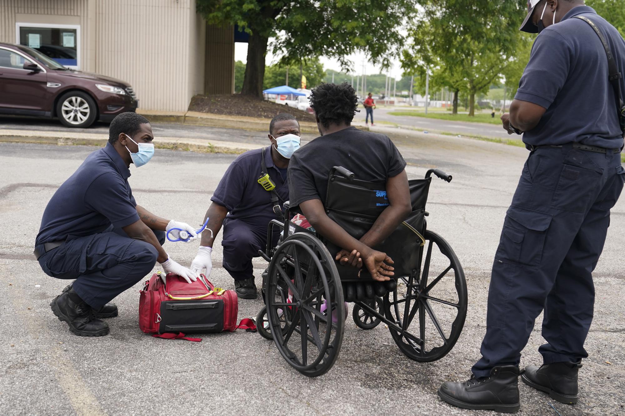 Paramedics help a man in distress in a parking lot in St. Louis on Saturday, May 22, 2021. He was found passed out in the middle of a busy parking lot. In the city of St. Louis, deaths among Black people increased last year at three times the rate of whites, skyrocketing more than 33% in a year. (AP Photo/Brynn Anderson)