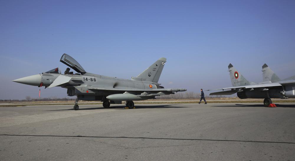 A military officer is passing between Bulgaria's MiG-29 and Spanish Eurofighter EF-2000 Typhoon II aircraft and MiG-29, in Graf Ignatievo, Thursday, Feb. 17, 2022.. As part of the united efforts of NATO partners to bolster the defense of the Alliance's eastern flank while tensions are continuing over a possible Russian invasion in Ukraine, Spain is sending fighter jets to Bulgaria to implement joint air policing missions. (AP Photo/Valentina Petrova)