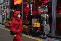 A woman wearing a mask to protect from the coronavirus walks past a coat of armour displayed outside a restaurant in Beijing, China, Friday, Jan. 21, 2022. The sweeping "zero-tolerance" policies that China has employed to protect its people and economy from COVID-19 may, paradoxically, make it harder for the country to exit the pandemic. (AP Photo/Ng Han Guan)