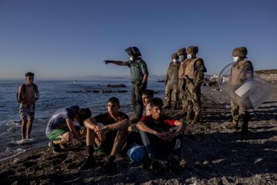 ARCHIVO - La foto de archivo del 19 de mayo de 2021 muestra a migrantes rodeados por agentes de policía españoles en una playa en el enclave español de Ceuta, cerca de la frontera con Marruecos. (AP Foto/Bernat Armangue, File)